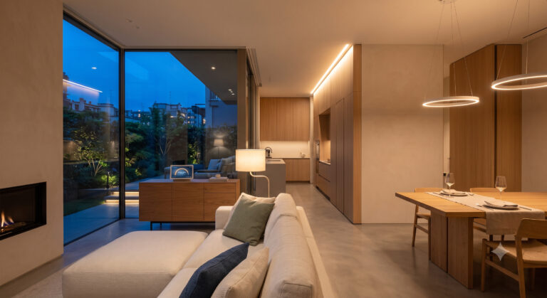 Illuminazione circadiana casa: soggiorno open space con luce biodinamica calda serale, gole LED indirette e vetrata sul crepuscolo progettato da Flow Line Studio.